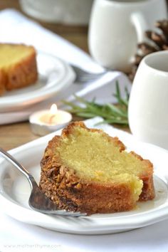 a piece of cake on a white plate with a fork next to it and a cup of tea in the background