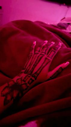 a person's hand with tattoos on it laying in bed under a purple light