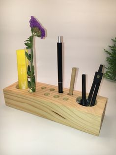 a wooden holder with pens, pencils and flowers in it on a white surface