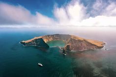 an island in the middle of the ocean with two boats floating on it's side