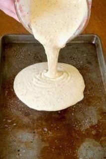 a person pouring batter on top of a cookie sheet