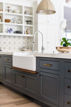 a kitchen with gray cabinets and white counter tops, an island sink and hanging lights