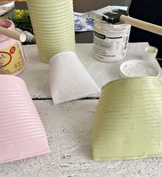 some paper cups are sitting on a table with paint and brushes in them, along with other craft supplies