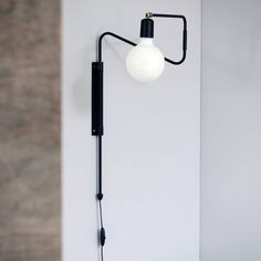 a black wall light with a white ball on the arm and an electrical cord attached to it