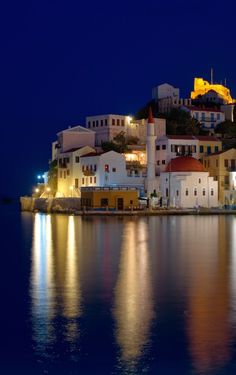 an island is lit up at night with buildings on it and lights reflecting in the water