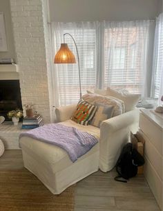 a living room with a white couch, chair and lamp on the floor in front of a window