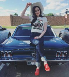 a woman sitting on the hood of a car wearing red shoes and a cowboy hat