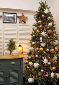 a decorated christmas tree sitting in front of a window next to a dresser and framed pictures