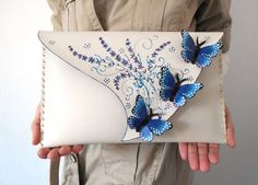 Unique cut white clutch with Morpho Butterflies and painted lavender flowers is a quirky and unique gift for people who love unusual purses.  You can also find more butterflies if you follow this link : https://www.etsy.com/shop/spiculdegrau?ref=hdr_shop_menu&section_id=21096579 Made of leather and hand cut leather pieces Hand painted and using collage technique. With magnetic clasp closure. The interior is fully lined with fabric. Detachable chain strap included - 120cm / 47in. Approximate dime Butterfly Purse, Unique Leather Bag, Painted Leather Bag, Butterfly Bag, Black Butterflies, Artisan Bag, Artist Bag, Pink Dragonfly, Painted Butterfly