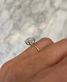 a woman's hand with a diamond ring on top of her finger, in front of a marble background