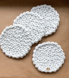 three crocheted white plates sitting on top of a brown table next to each other