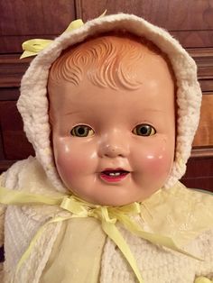 an old fashioned baby doll wearing a white dress and yellow bow around its neck, with eyes wide open