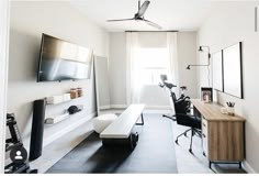 a room with a desk, chair and television on the wall next to a window