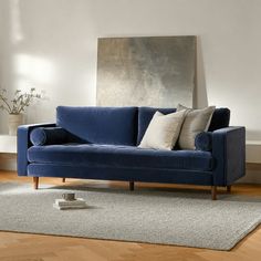 a blue couch sitting on top of a wooden floor next to a white rug and wall