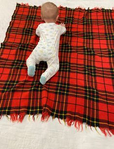 a baby laying on top of a red and black plaid blanket