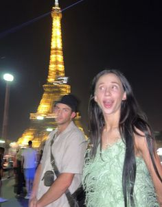 a man and woman standing in front of the eiffel tower with their hair blowing in the wind