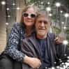 an older man and woman hugging each other in front of string lights on the wall