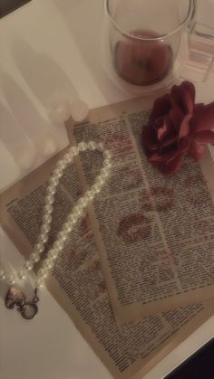 an old book with pearls and a rose on it next to a glass of water