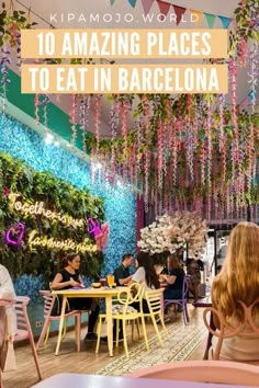 the inside of a restaurant with flowers hanging from the ceiling and people sitting at tables