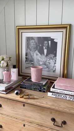 a dresser topped with books and vases next to a framed photograph on the wall