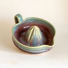 a green and purple ceramic bowl with a lid on it's side, sitting on a white surface