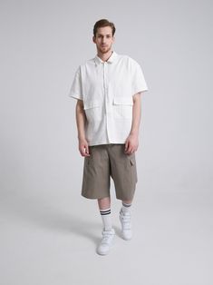 a man standing in front of a white background wearing shorts and a shirt with pockets