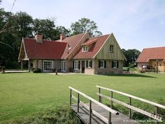 a wooden bridge crossing across a lush green field next to two small houses with red roofs