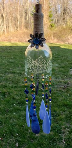 a wine bottle wind chime hanging from a tree in the grass with leaves and flowers on it