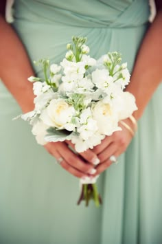 a woman in a green dress holding a bouquet of white flowers on her wedding day