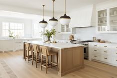 a large kitchen with white cabinets and wooden flooring, along with two pendant lights hanging from the ceiling