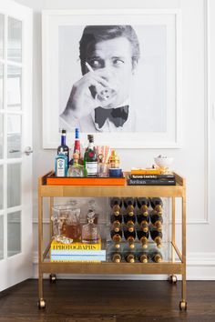 a bar cart with bottles and liquor on it in front of a framed photo,