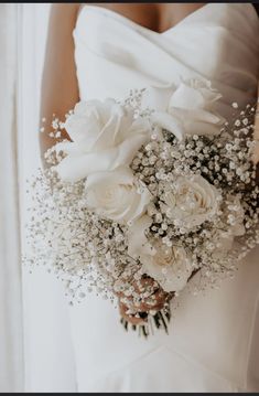 a bride holding a bouquet of white roses and baby's breath in her hand