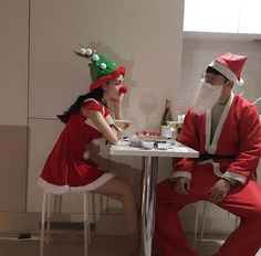 two people dressed up as santa and mrs claus sitting at a table