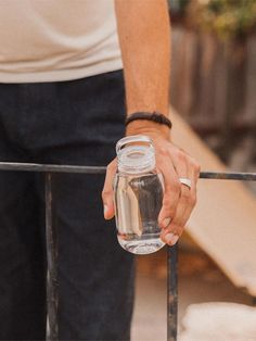 a man holding a glass jar with water in it on top of a metal railing