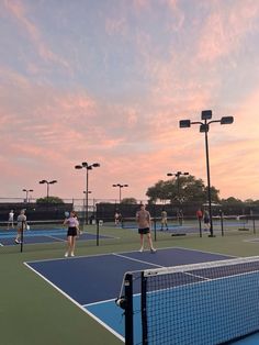 people playing tennis on an outdoor court at sunset