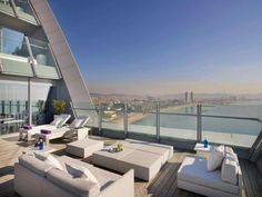 a balcony with white couches and chairs overlooking the cityscape in the distance