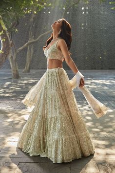 a woman in a white and gold gown standing on the sidewalk with trees behind her