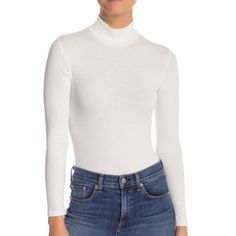 a woman is wearing a white turtle neck sweater and blue denim jeans with her hands in her pockets