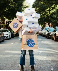 a woman carrying several boxes on her head while standing in the middle of an empty street