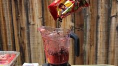 a blender filled with red liquid sitting on top of a table next to a wooden fence