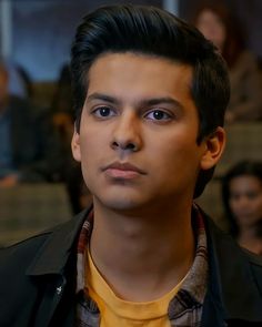 a close up of a person wearing a yellow shirt and black jacket with people in the background