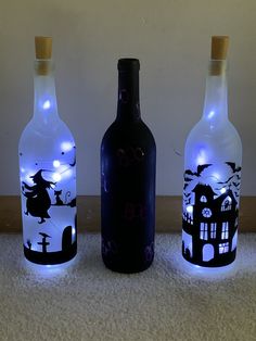 three wine bottles decorated with halloween images and light up corks are sitting on the floor