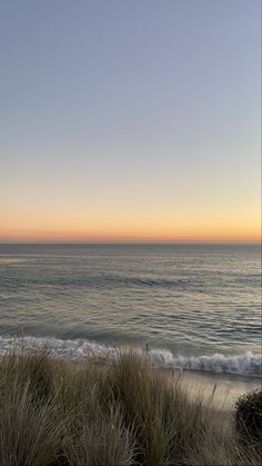 an ocean view with the sun setting on the horizon and grass in the foreground