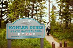 a sign for kohler dunes state natural area with people walking in the background