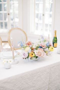 a table topped with a vase filled with flowers next to a wine bottle and candle