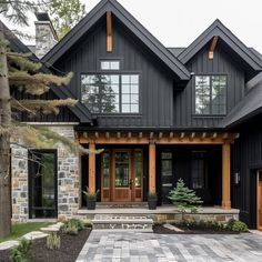 a large black house with wood trimming and stone walkway leading to the front door