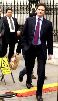 a man in a suit and tie walking down the street with other people behind him