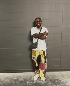 a man standing in front of a wall wearing headphones and colorful pants with his arms crossed