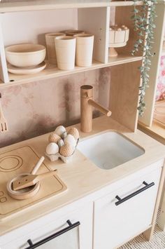 a toy kitchen with wooden utensils on the counter top and shelves above it