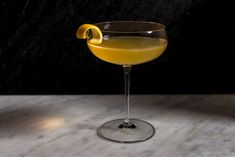 a glass filled with yellow liquid sitting on top of a marble counter next to a black wall